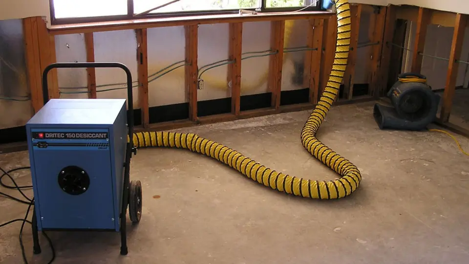 Dehumidifier and drying hose set up beside opened wall studs after a leak